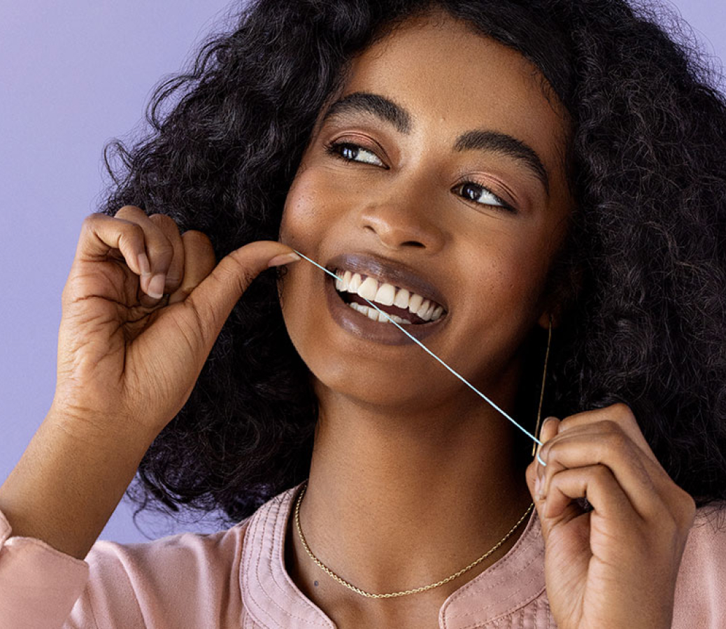 A portrait of a smiling woman flossing her two front teeth.